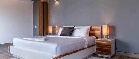 A modern bedroom with a large bed, wooden headboard, bedside lamps, and a neutral color scheme.