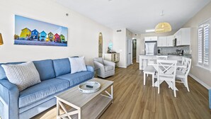 Un saló modern amb un sofà blau, una taula de centre de fusta i una zona de menjador amb cadires blanques i una taula.