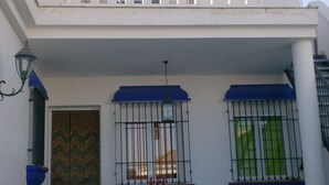 A building with a white facade, a balcony with white balustrades, and a blue awning over the entrance. - El Mirador de Pablo, Casa con Patio Privado (Alomartes)