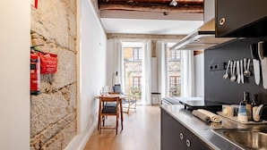 A modern kitchen with a stone wall, wooden dining table, and a view of the courtyard. - Artes, the Studio in Porto World Heritage (Porto)