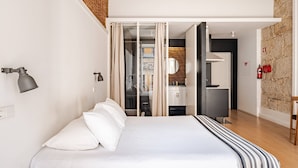 A modern hotel room with a large bed, a desk, and a bathroom visible through a glass partition. - Artes, the Studio in Porto World Heritage (Porto)