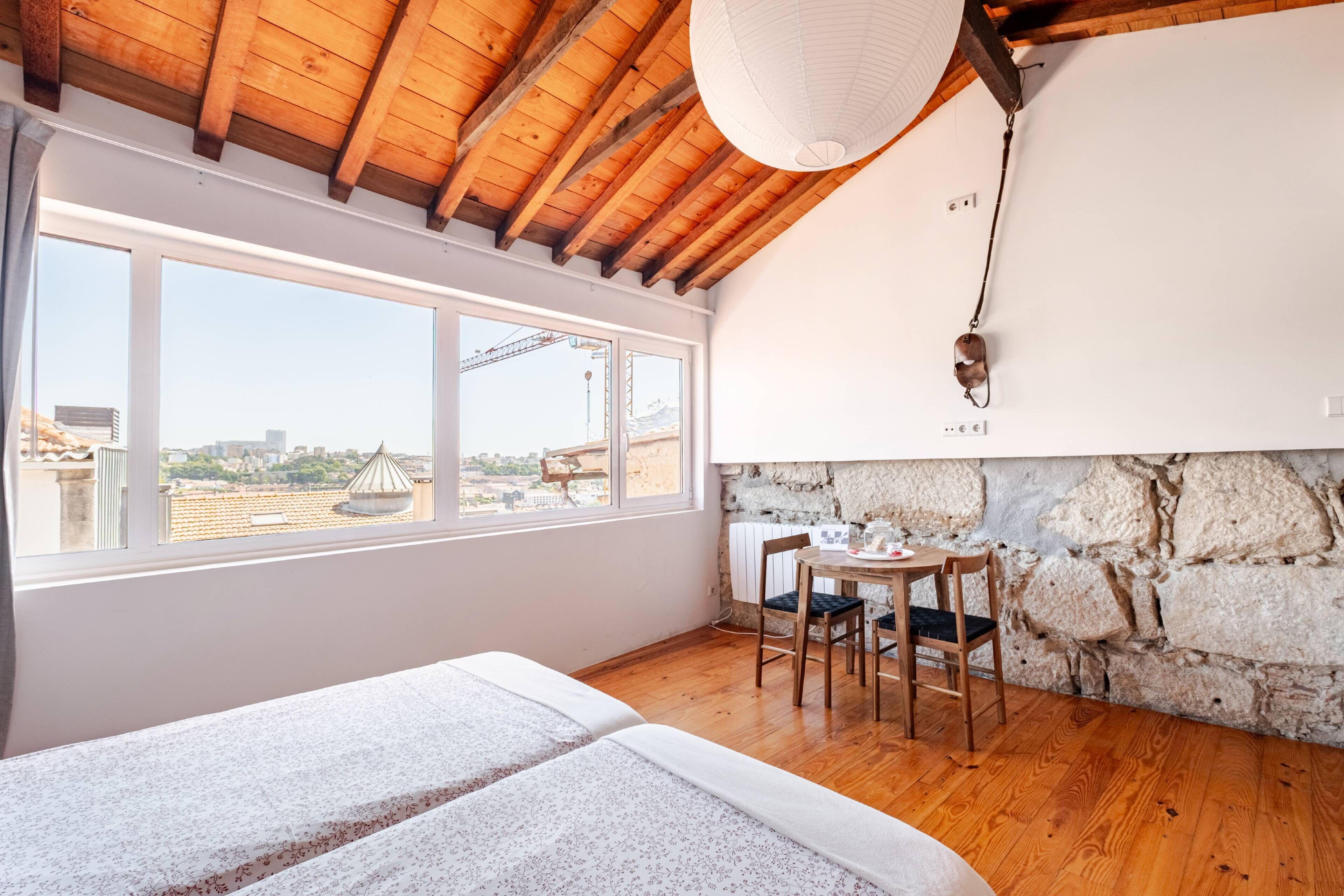 A room with a wooden ceiling, large windows, a stone wall, and a small table with chairs.