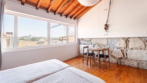 Una habitación con techo de madera, ventanas amplias, pared de piedra y una pequeña mesa con sillas.