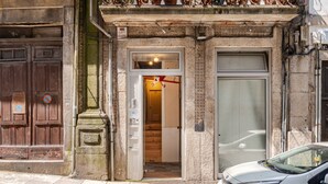 Un edificio con una puerta de madera, una puerta de vidrio y un coche blanco estacionado en la entrada.