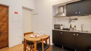 Una cocina compacta con armarios oscuros, un microondas y un lavamanos. Hay una mesa de comedor de madera con sillas y una ventana pequeña.