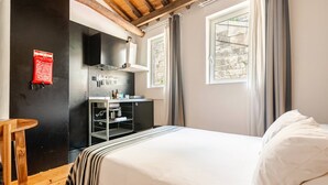 Ein Schlafzimmer mit einem Bett, einem Holzstuhl, einer Küchenzeile und einem Fenster mit Vorhängen.