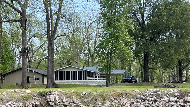 A lakeside cabin with a dock, surrounded by trees and a stone wall. - Peak Season! Arkansas River Cabin with Dock,White Bluff Views, Fishing & Sandbar (Tucker)
