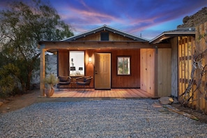 A wooden cabin with a covered patio, a door, and a window.