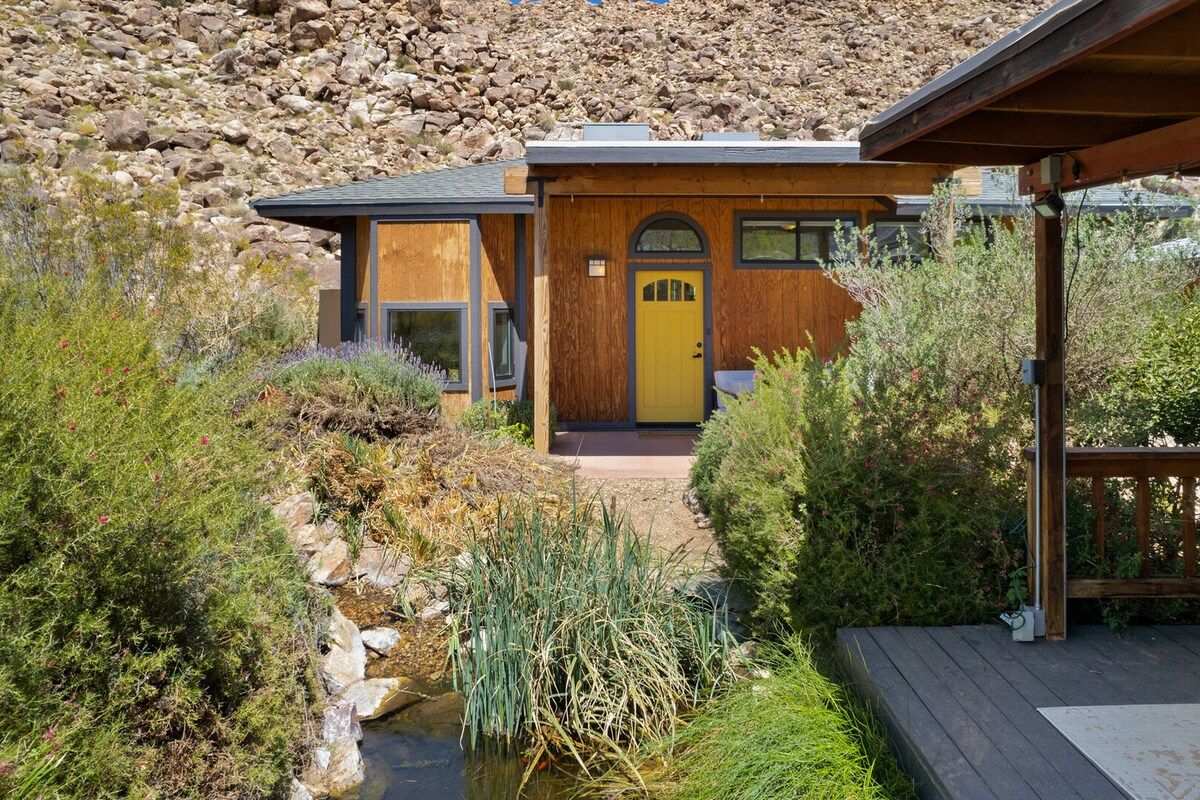 A modern house with a wooden exterior, a yellow door, and a small garden with a pond.