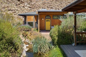 A modern house with a wooden exterior, a yellow door, and a small garden with a pond. - Moonbeam Mountain - Stylish Suites + Hot Tub (Joshua Tree)