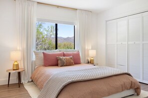 Un dormitorio con una cama grande, dos mesitas de noche con lámparas, una ventana con cortinas y un armario.