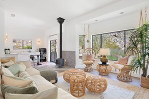 A spacious living area with a sofa, rattan chairs, and a fireplace. - Moonbeam Mountain - Stylish Suites + Hot Tub (Joshua Tree)