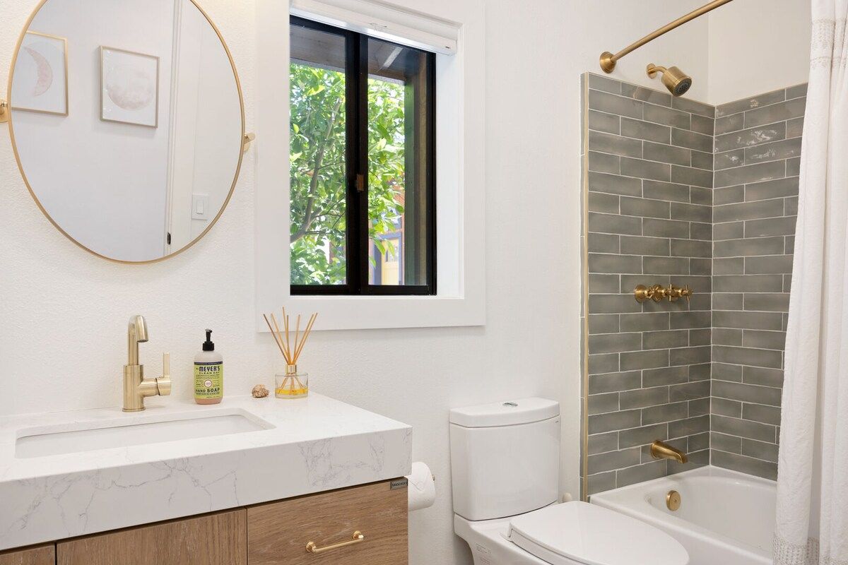 A bathroom with a white sink, gold fixtures, a toilet, and a shower with grey tiles.