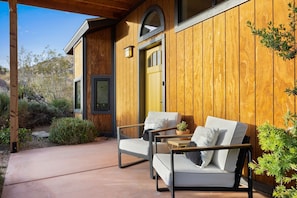 A wooden exterior with a yellow door, two chairs with cushions, and a small table with a plant. - Moonbeam Mountain - Stylish Suites + Hot Tub (Joshua Tree)