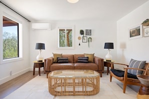 A living room with a brown leather sofa, a glass coffee table, and a wicker side table.