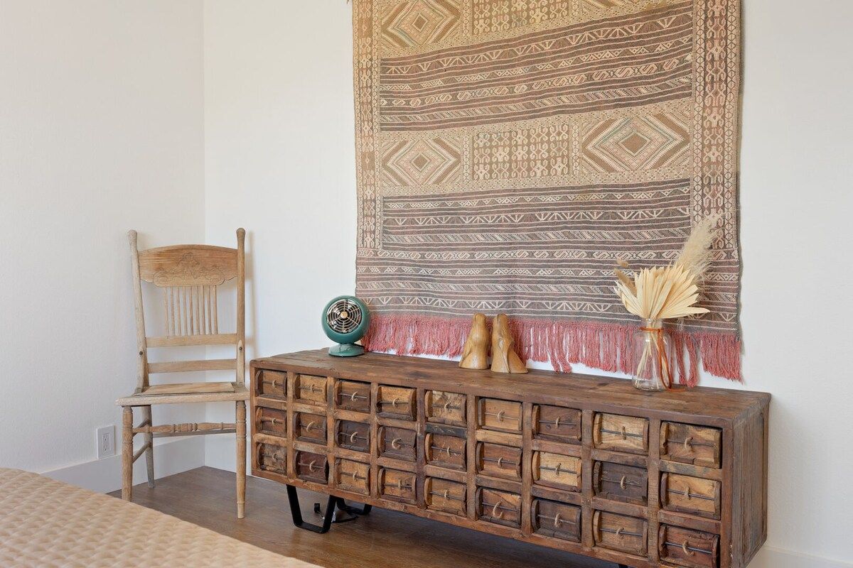 Une pièce comprenant une chaise en bois, une commode en bois avec des tiroirs et une tapisserie à motifs accrochée au mur.