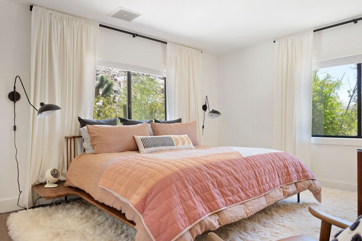A bedroom with a bed, white curtains, a window, and a white furry rug.