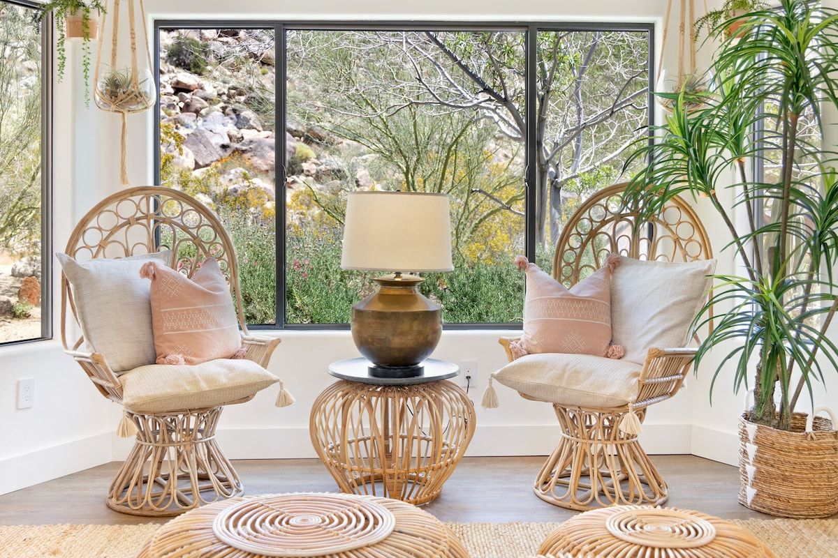 A room with two wicker chairs, a table with a lamp, and a potted plant.
