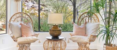 A room with two wicker chairs, a table with a lamp, and a potted plant.