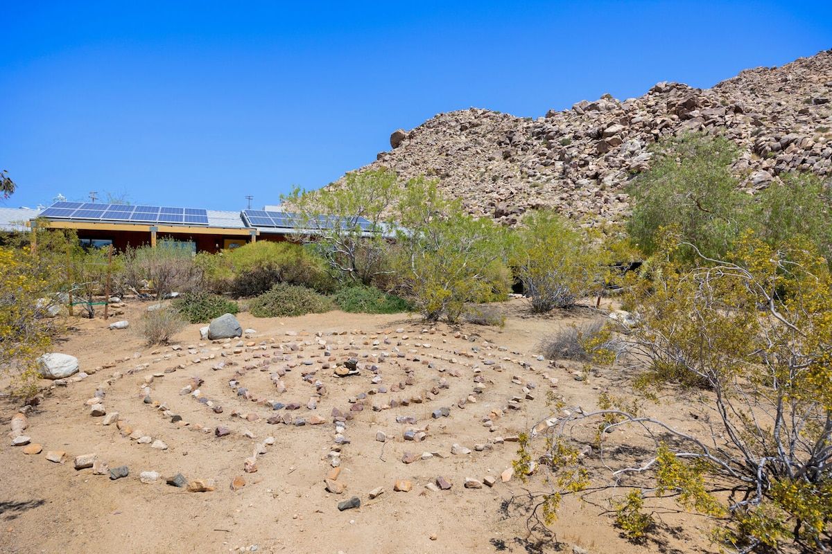 A desert landscape with a building featuring solar panels, a rock maze, and sparse vegetation.