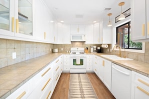 A modern kitchen with white cabinetry, a central island, and a patterned rug. - Moonbeam Mountain - Stylish Suites + Hot Tub (Joshua Tree)