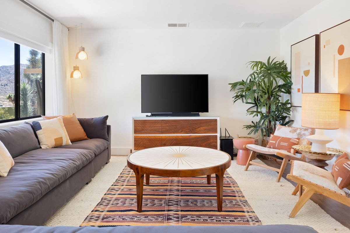 A modern living room with a sofa, a round coffee table, a television, and a large plant.