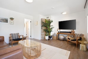 A modern living room with a large flat-screen TV, a round glass coffee table, and two sofas.