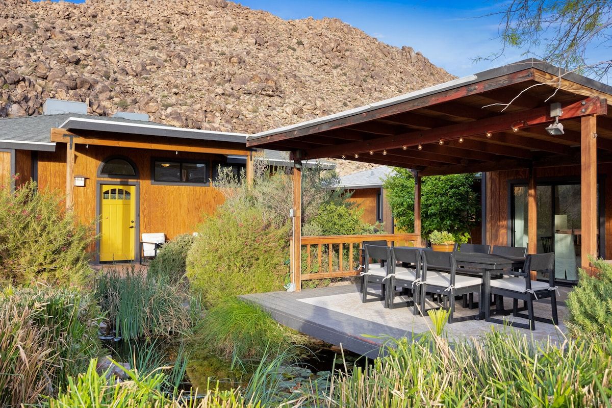 A building with a wooden exterior, a yellow door, and a covered outdoor seating area with tables and chairs.