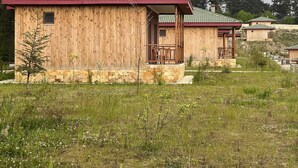 A wooden cabin with a green tiled roof, situated in a grassy area with trees in the background.