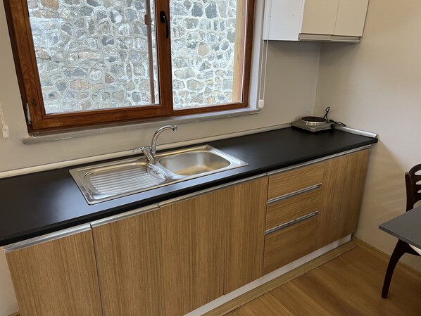 A kitchen with a double sink, wooden cabinets, and a stone wall visible through the window.