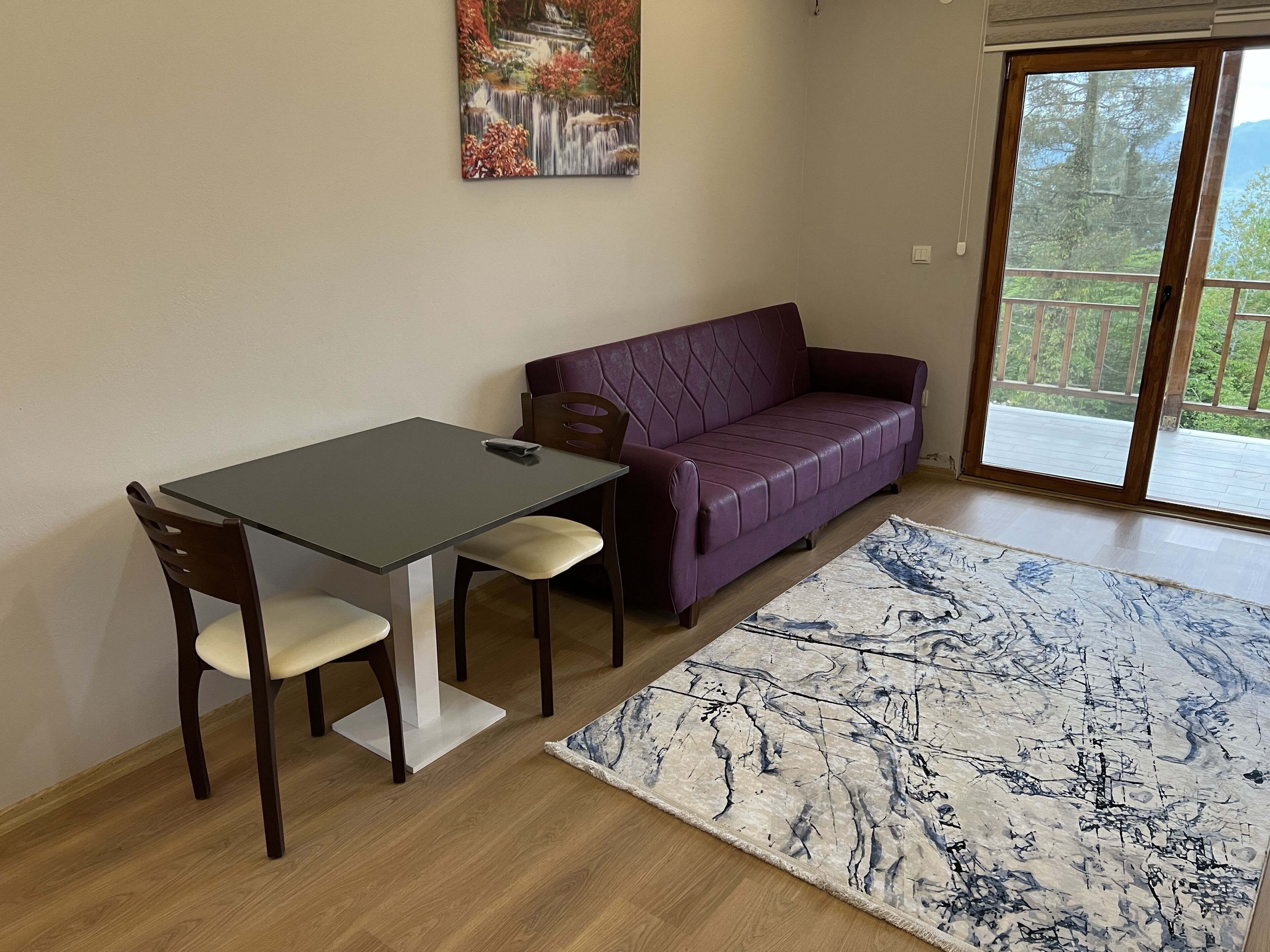 Una habitación con una mesa de comedor, dos sillas, un sofá púrpura y un ventanal grande.