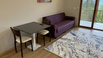 Una habitación con una mesa de comedor, dos sillas, un sofá púrpura y un ventanal grande.
