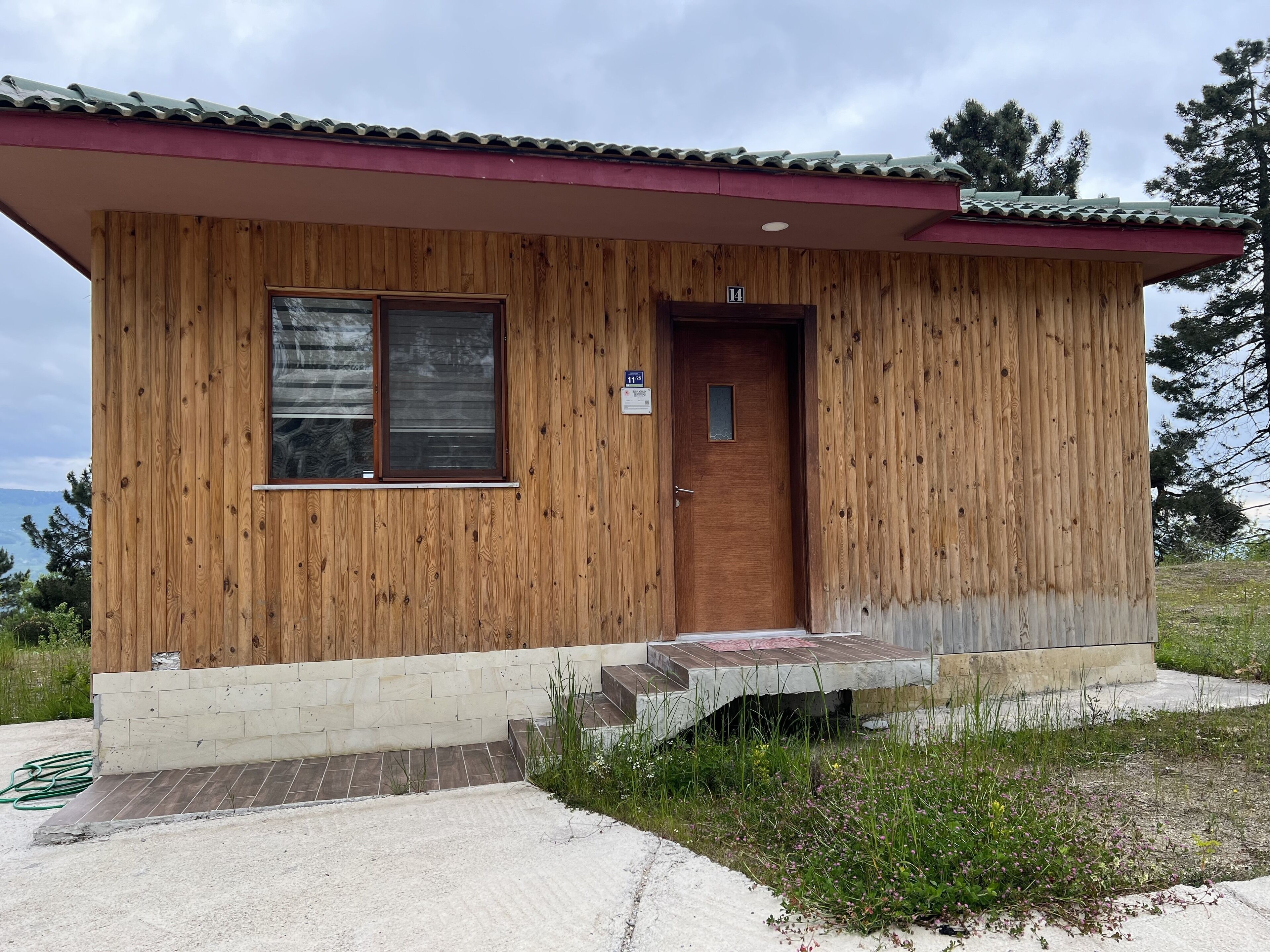 Eine kleine Holzhütte mit einer Tür und einem Fenster, Nummer 14, mit einer Betonplattform, die zum Eingang führt.