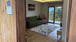 A living room with a green sofa, a pink armchair, a large window, and a painting on the wall.