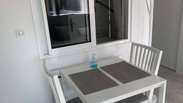 A white dining table with two chairs, a window with a view of the outside, and a floor lamp.