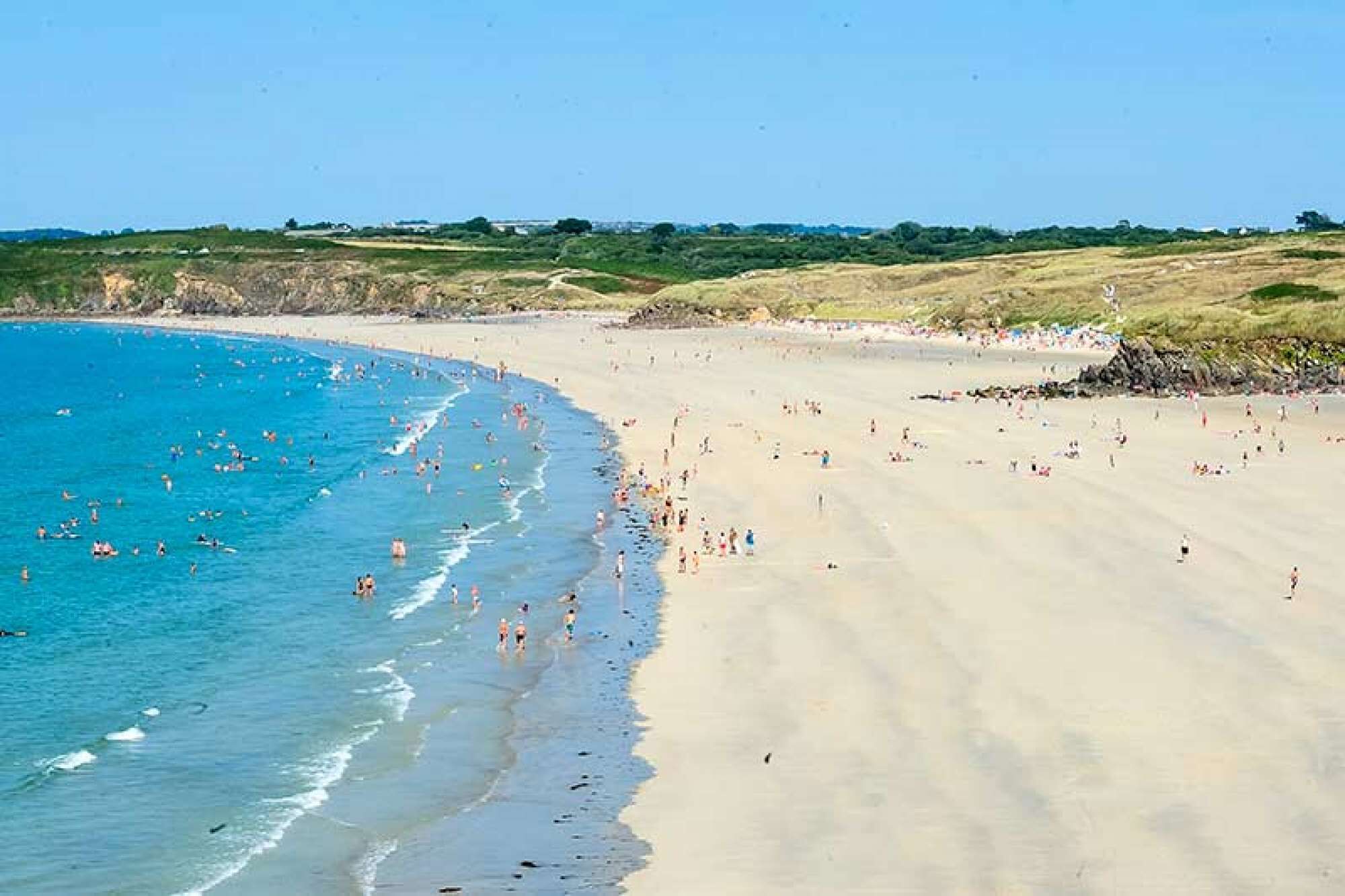 A beach with people swimming and sunbathing.