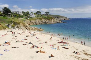 Une plage où l’on peut se détendre au soleil et se baigner, des maisons situées sur une colline et un ciel dégagé.