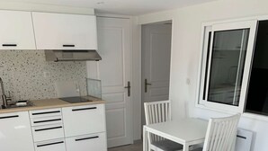 Cocina compacta con armarios blancos y una encimera, una mesa de comedor con sillas y un sofá con cojines.
