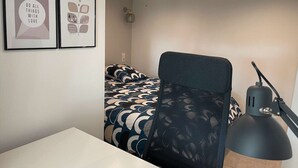 Una habitación pequeña y moderna con una cama, un escritorio y una silla. Hay dos cuadros en la pared.