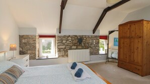 Ein Schlafzimmer mit Steinwand, Holzschrank, Bett mit gemusterten Betttextilien und einem Fenster mit Blick.