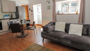Ein modernes Wohnzimmer mit grauem Sofa, einem Esstisch mit Stühlen, einer Küchenzeile mit Schränken und einem Fenster mit Vorhängen.
