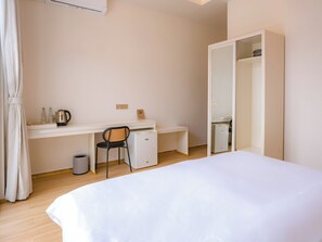 A bedroom with a bed, a desk, a chair, a small refrigerator, and a wardrobe.