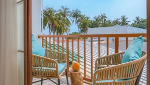 A balcony with wicker chairs and a wooden post, overlooking a rooftop with a view of palm trees and buildings. - Thundi village and spa (Maalhos)