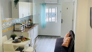 Een compacte keuken met witte kastjes, een magnetron en een klein eethoekje met een tafel en stoelen.