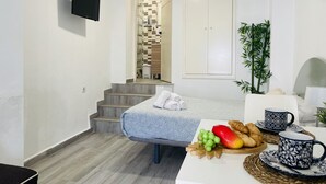 Een hotelkamer met een bed, een klein tafeltje met ontbijtartikelen, een aan de muur bevestigde televisie en een trap naar een badkamer.