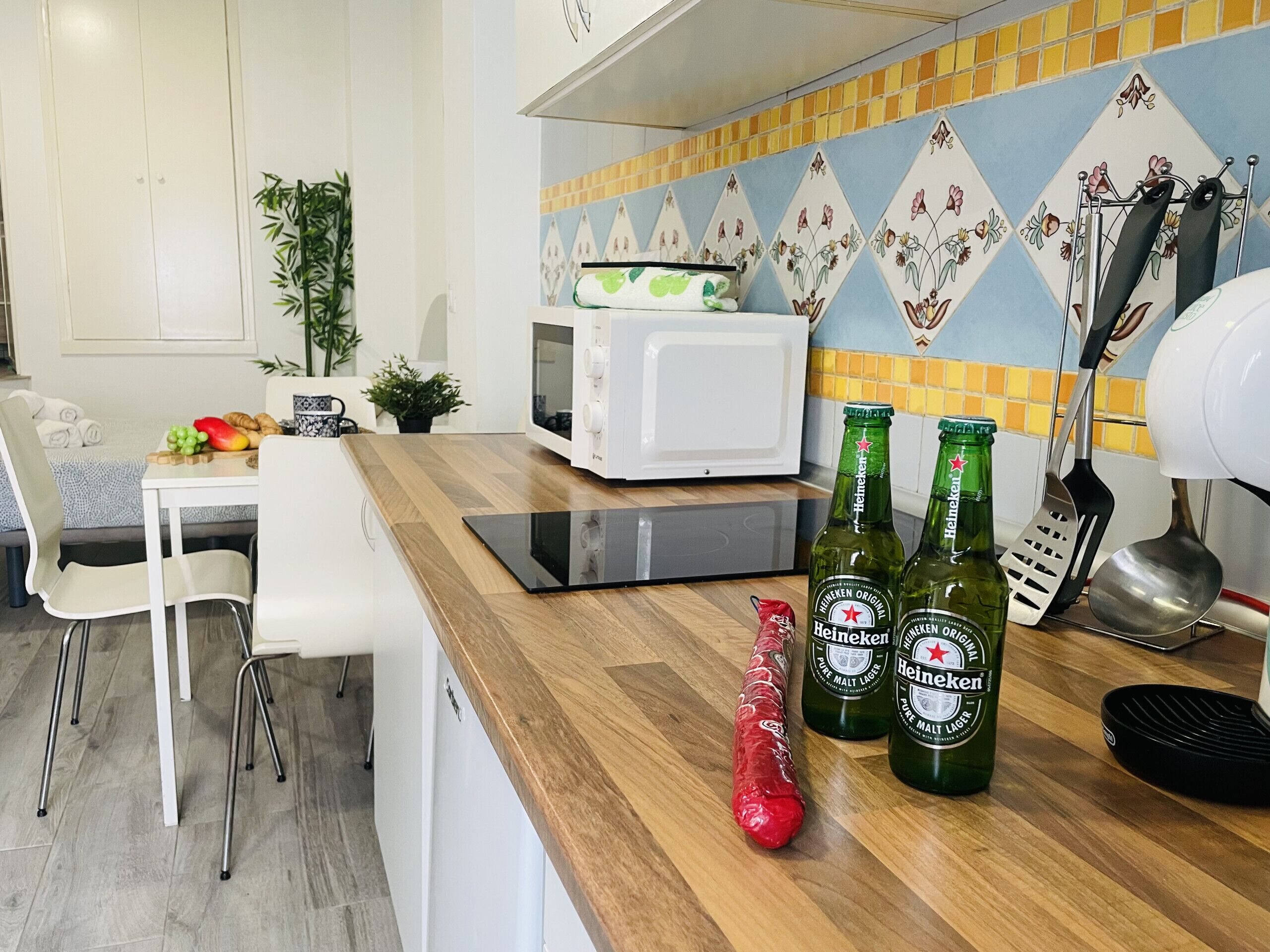 Une cuisine équipée d’un four à micro-ondes, de deux bouteilles de bière Heineken, d’un moulin à poivre rouge et d’une spatule posés sur le comptoir.