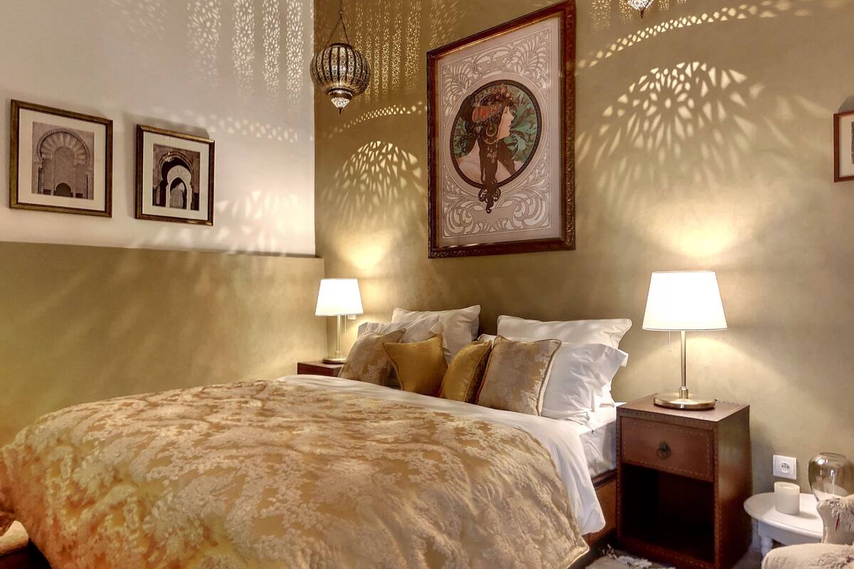 A bedroom with a large bed, two bedside tables with lamps, and framed pictures on the walls.