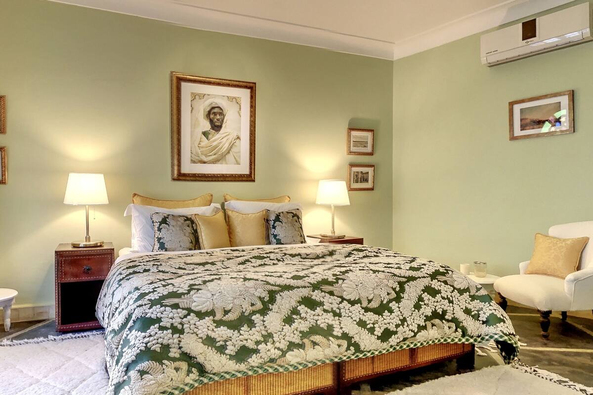 A bedroom with a large bed, two bedside tables with lamps, a chair, and framed pictures on the walls.