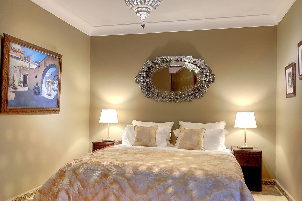 A bedroom with a large bed, two bedside tables, a mirror, and a painting on the wall.