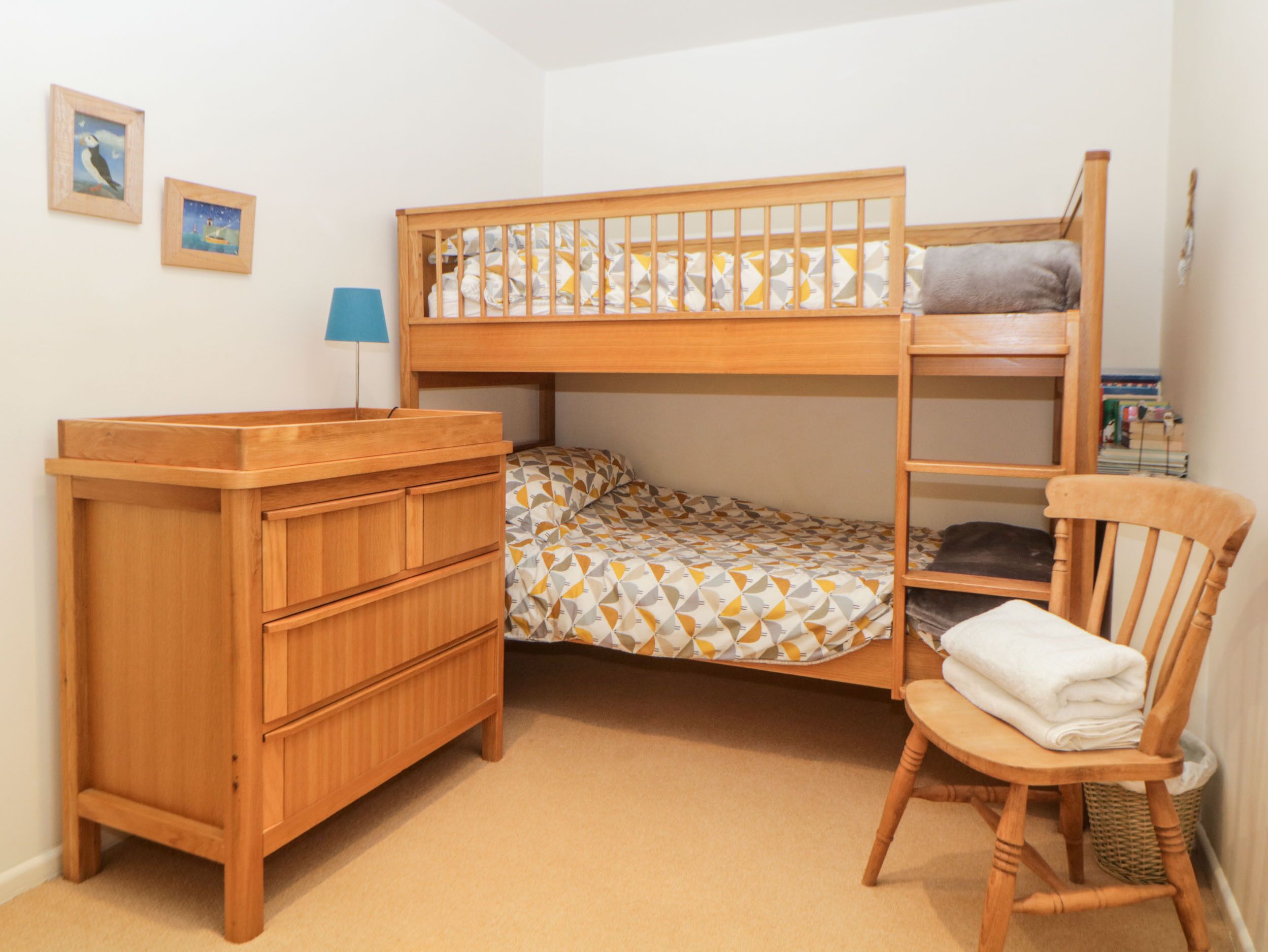 A bunk bed room with a wooden dresser, a chair, and two framed pictures on the wall.
